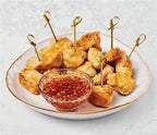 Bite-sized Chicken or tofu pieces on toothpicks with Sweet Chili Sauce by Epicure in a bowl on a white plate.