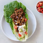 Lettuce wrap with taco beef, cheese, and vegetables on a white plate with a side of pico de gallo.